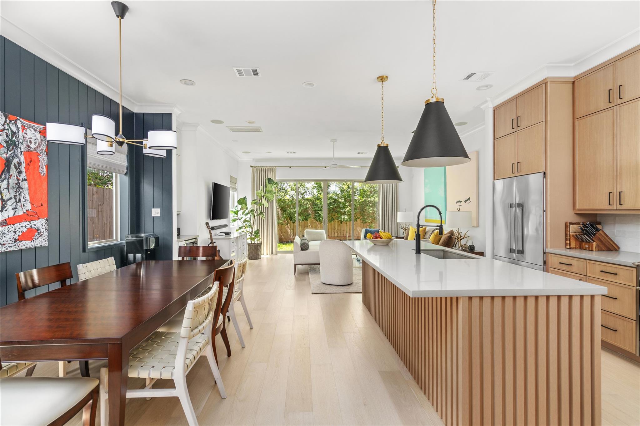 Open kitchen and dining area with a long island, wood cabinetry, and dark paneled accent wall.