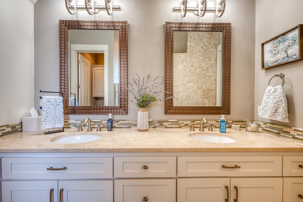 Bathroom double vanity with cream stone counter, white cabinetry, and two bronze-framed mirrors.