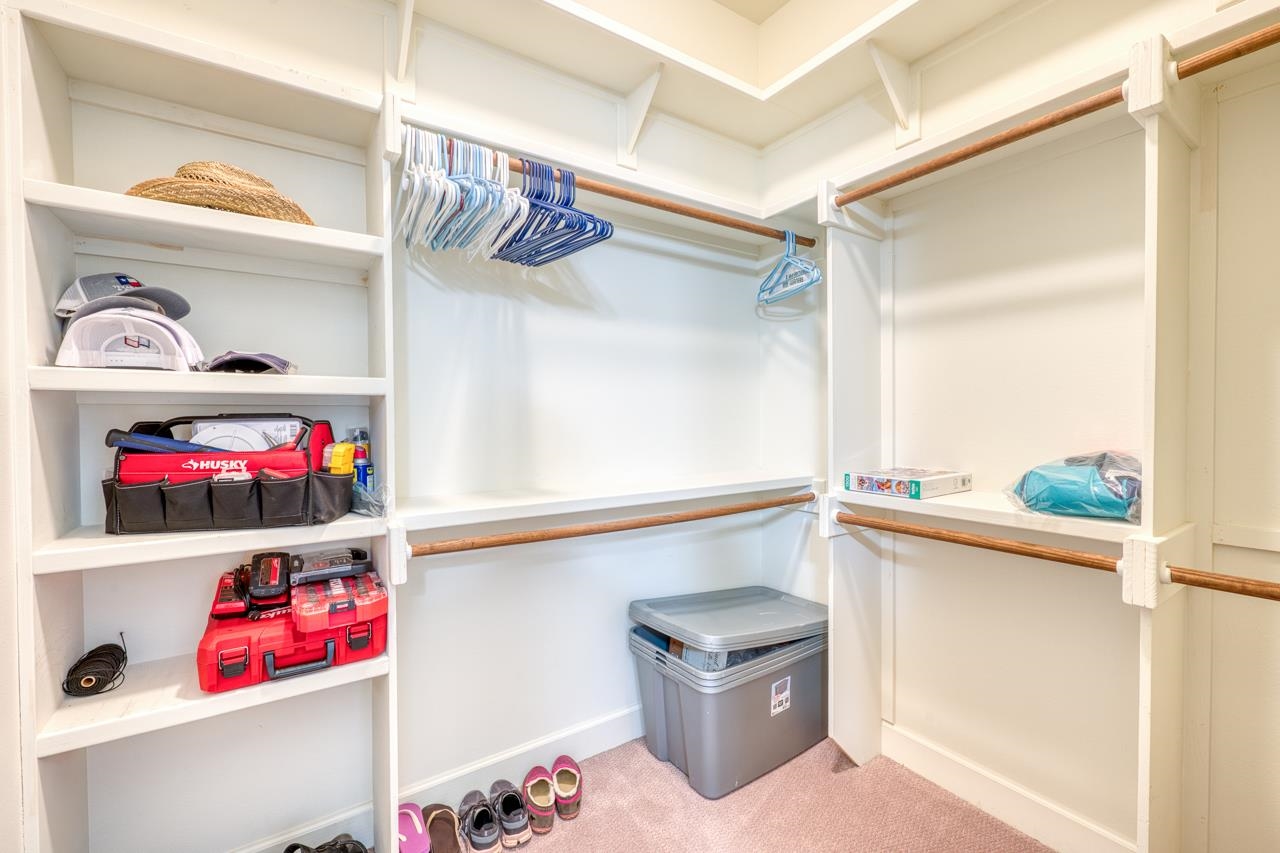 Walk-in closet with built-in shelves, wooden hanging rods, and storage items.