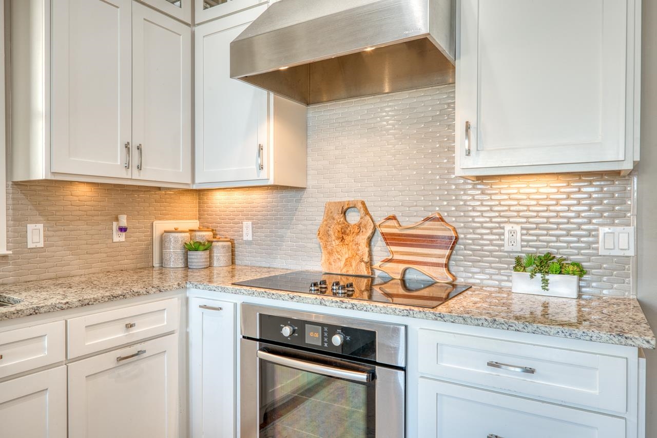 Modern kitchen with white cabinets, gray tile backsplash, and granite counters.
