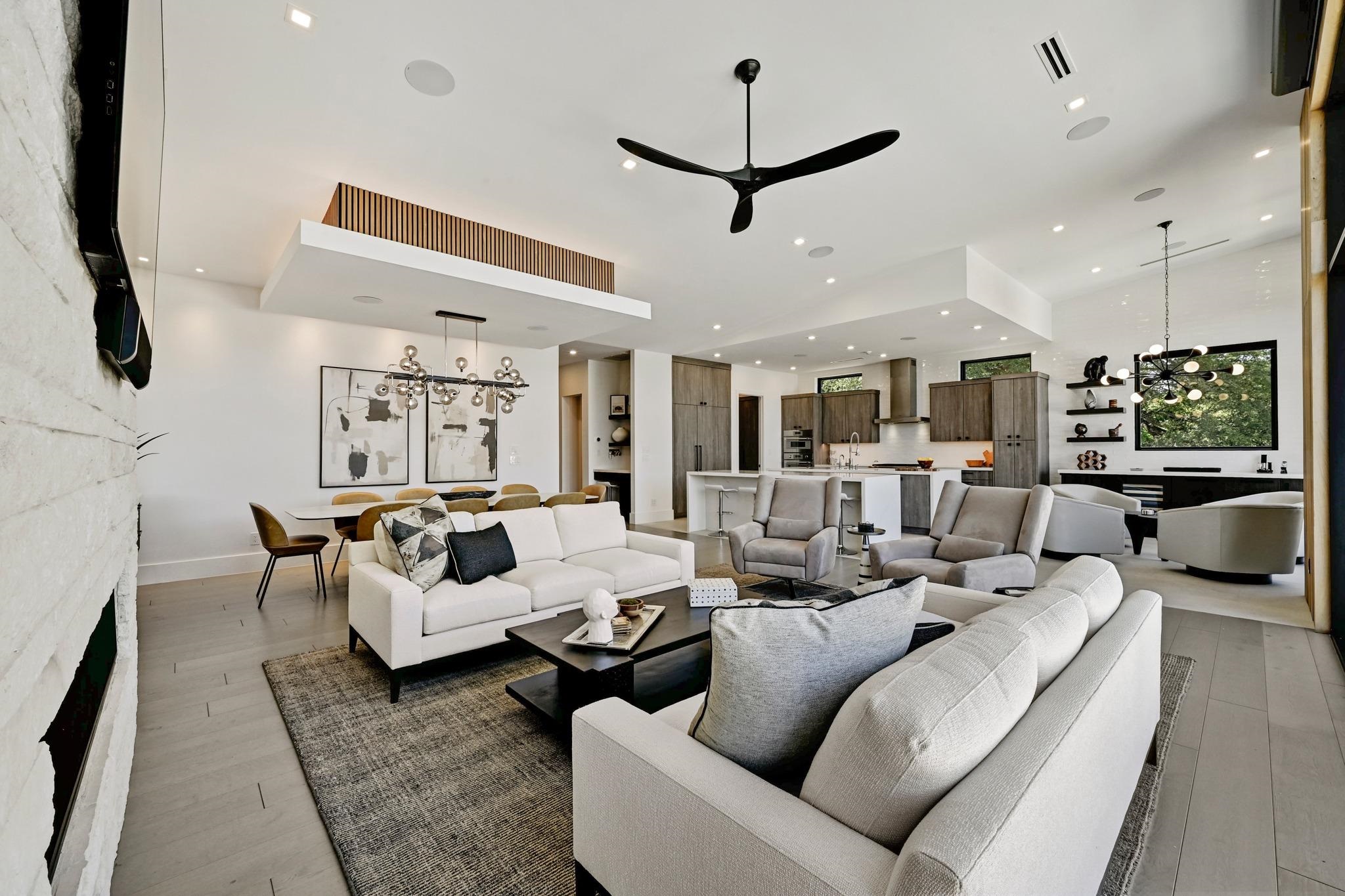 Open-plan living room with modern seating, dining area, and kitchen beneath a high ceiling.