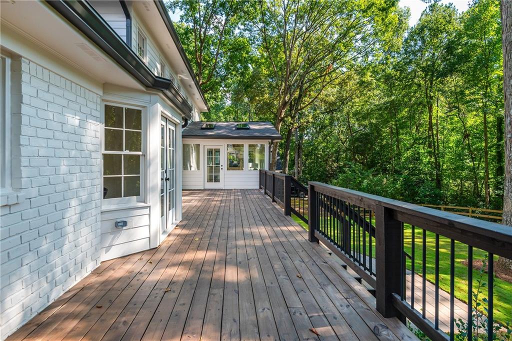 Wooden deck along a white house, with dark railings and a wooded yard beyond.