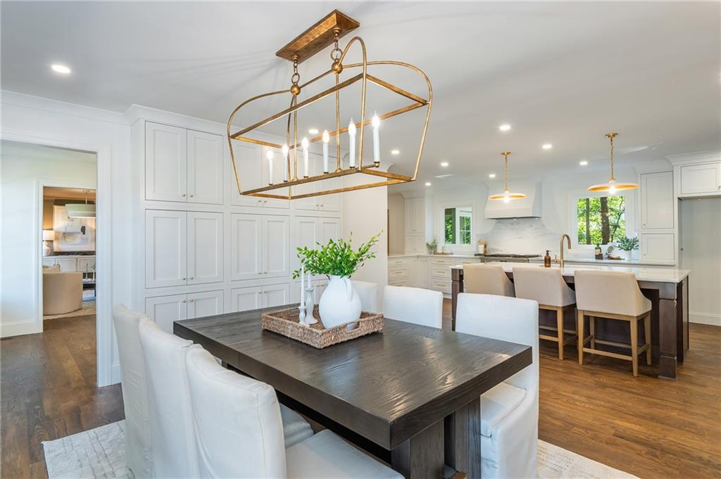 Dining room with a dark table and brass chandelier beside a bright white kitchen.