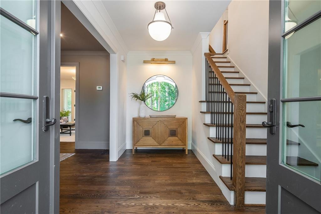 Entry foyer with hardwood floors, a round mirror above a console, and a wood-and-black staircase.
