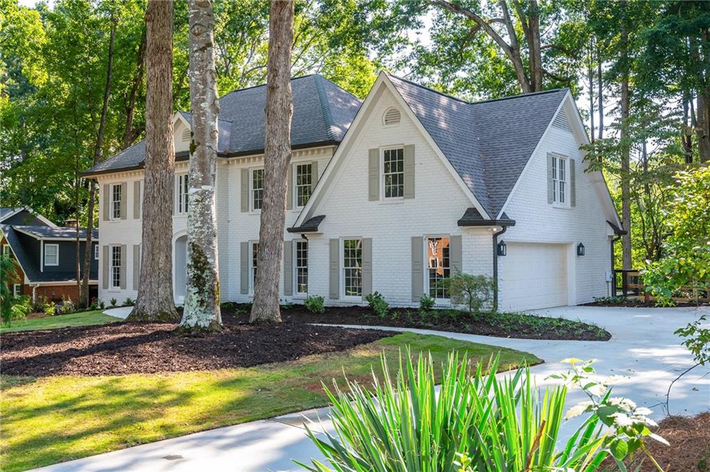 White brick home with multiple gables and a two-car garage, framed by mature trees.
