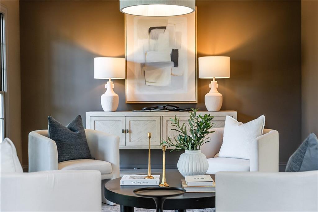 Staged living room with white armchairs, a dark coffee table, and abstract art above a light wood console.