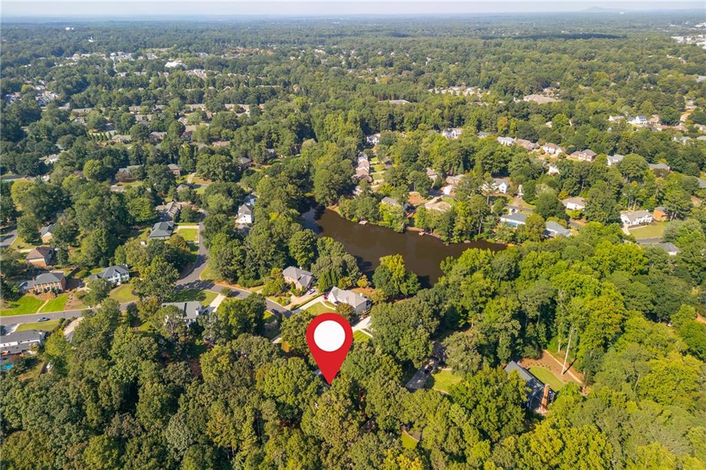 Aerial view of a wooded residential neighborhood, with a lake and property location marker.