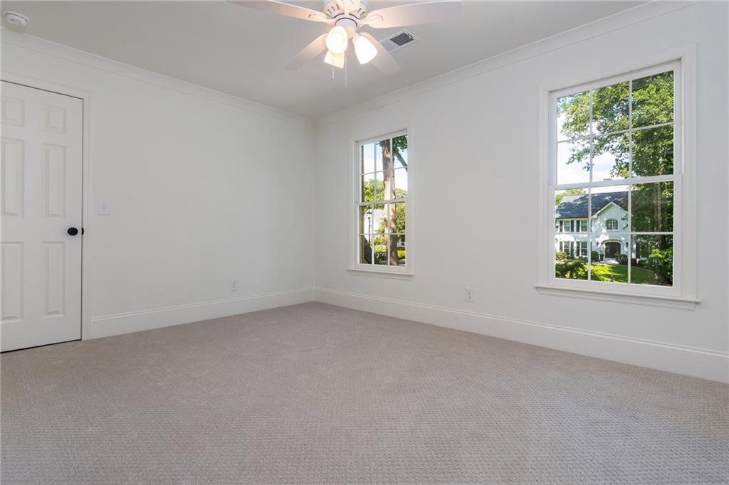 Vacant carpeted bedroom with a ceiling fan and two windows overlooking trees and a neighboring house.