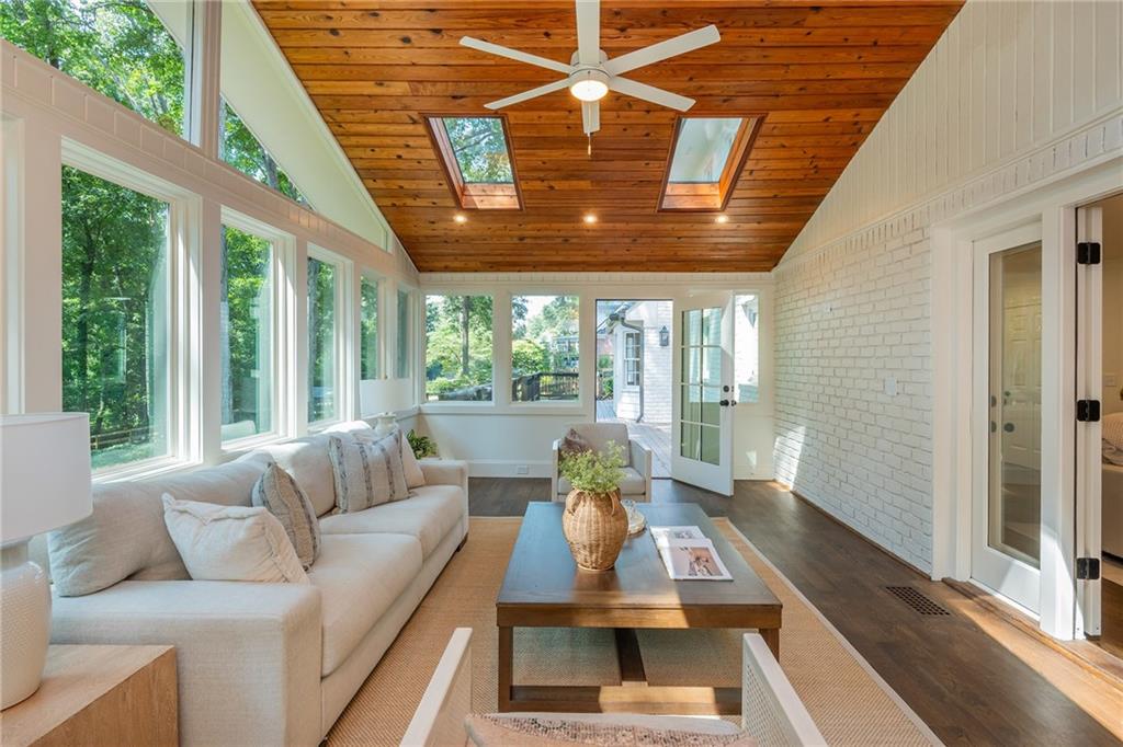 Sunroom with a vaulted wood ceiling, skylights, and tall windows overlooking trees.