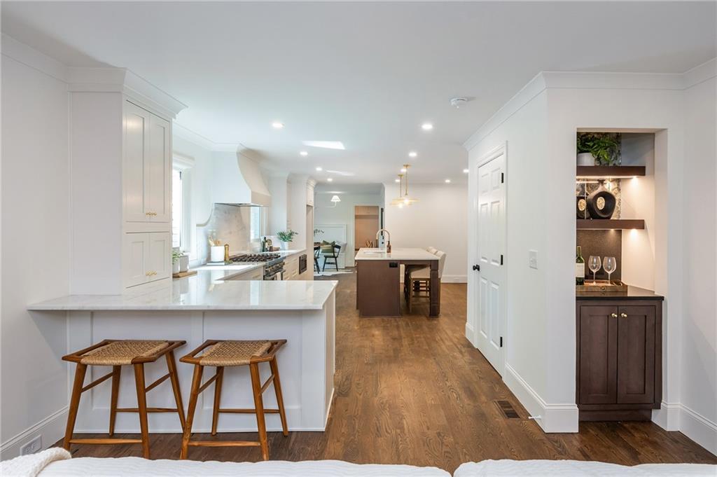 Kitchen with white cabinetry, a marble-look breakfast bar, woven stools, and a built-in wine bar.