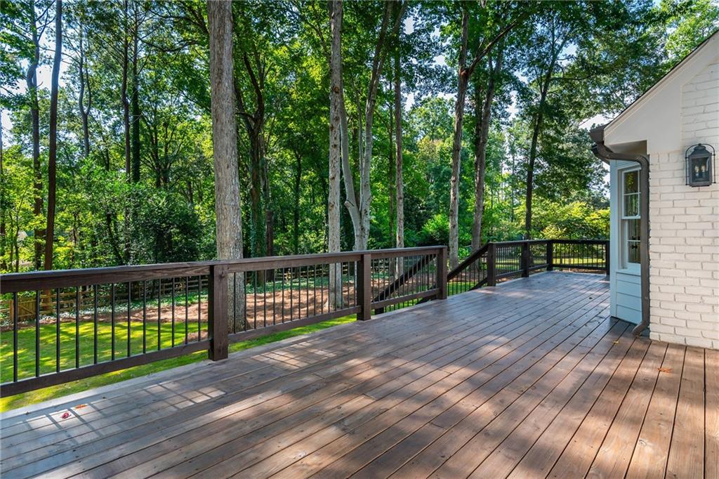 Wood deck with dark railings overlooking a green lawn and mature trees.
