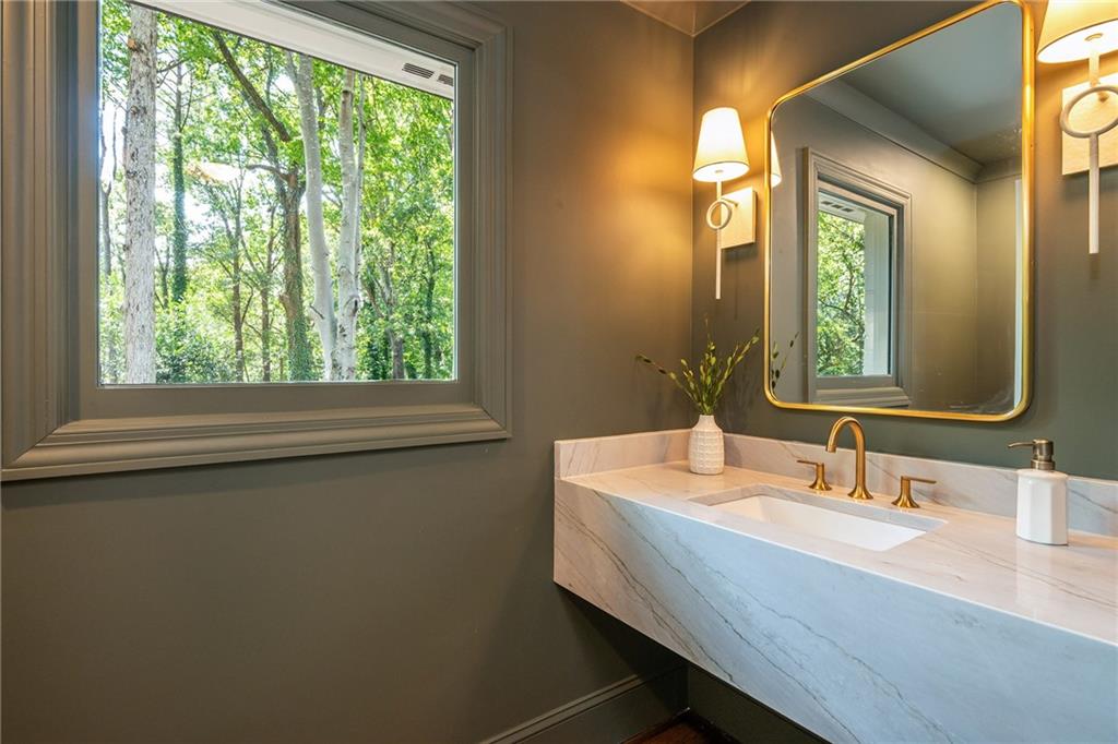 Bathroom with a floating marble vanity, gold fixtures, and a wide window overlooking trees.