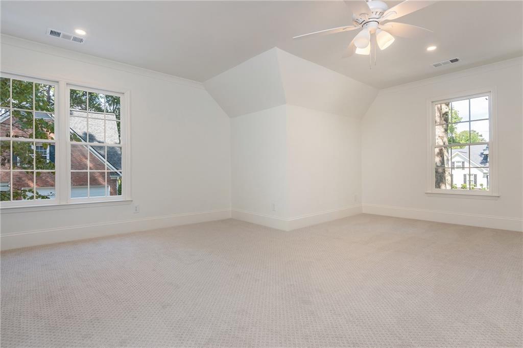 Vacant carpeted bedroom with a vaulted ceiling, ceiling fan, and three windows.