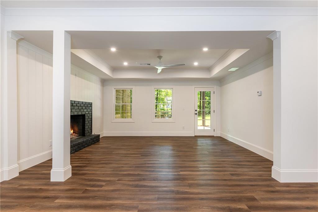 Empty living room with dark wood floors, a black brick fireplace, and a tray ceiling.