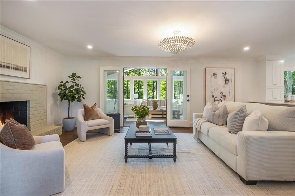 Living room with a white brick fireplace, neutral seating, and glass doors to a sunroom.