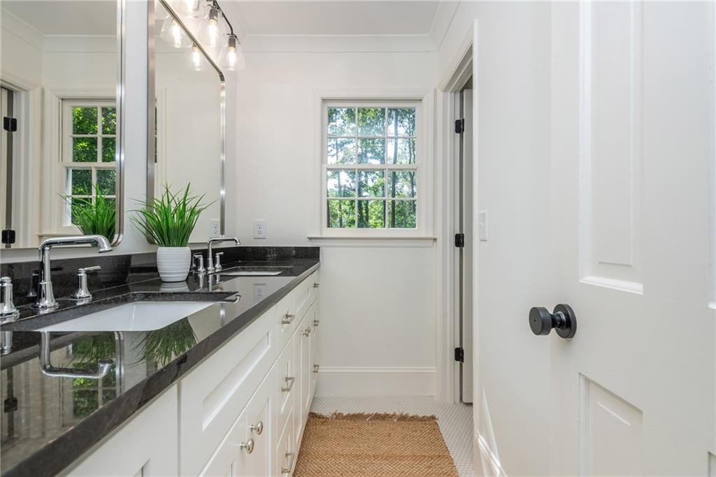 Bathroom with a white double vanity, dark stone countertop, and windows overlooking greenery.