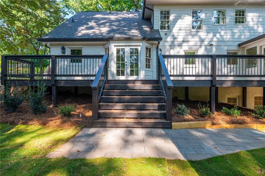 White two-story home with a raised deck, central stairs, and paved patio.