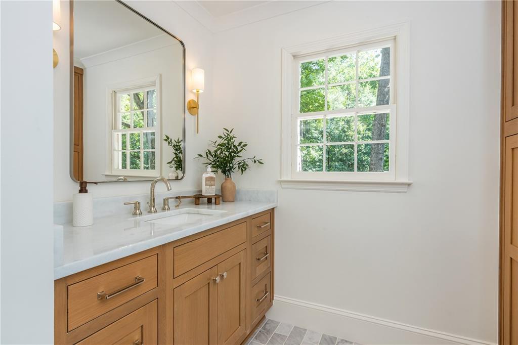 Bathroom vanity with light wood cabinets, a large mirror, and a sunlit window.