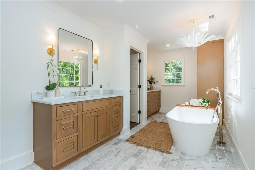 Bright bathroom with a wood double vanity and freestanding tub beside large windows.