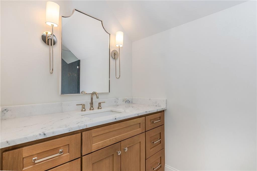 Bathroom vanity with a marble counter, rectangular sink, warm wood cabinets, and a framed mirror.