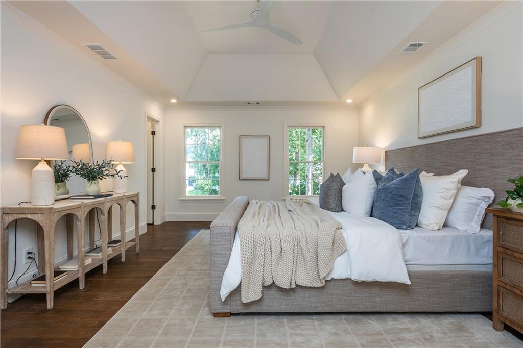 Furnished bedroom with an upholstered bed, blue accent pillows, tray ceiling, and two windows.