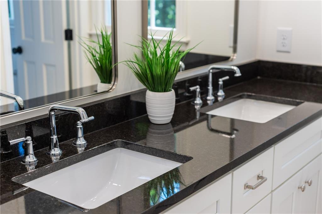 Bathroom vanity with double sinks, dark stone counters, chrome faucets, and white cabinetry.