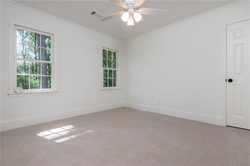 Empty bedroom with beige carpet, two windows, and a ceiling fan.