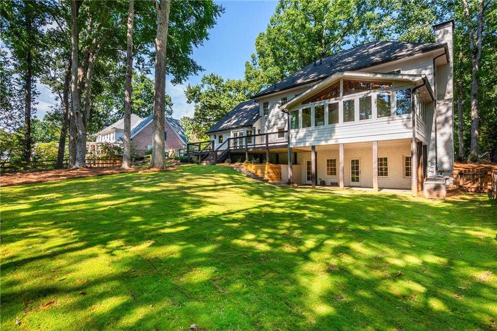 Rear of a multi-level house with a raised deck and broad, tree-shaded lawn.