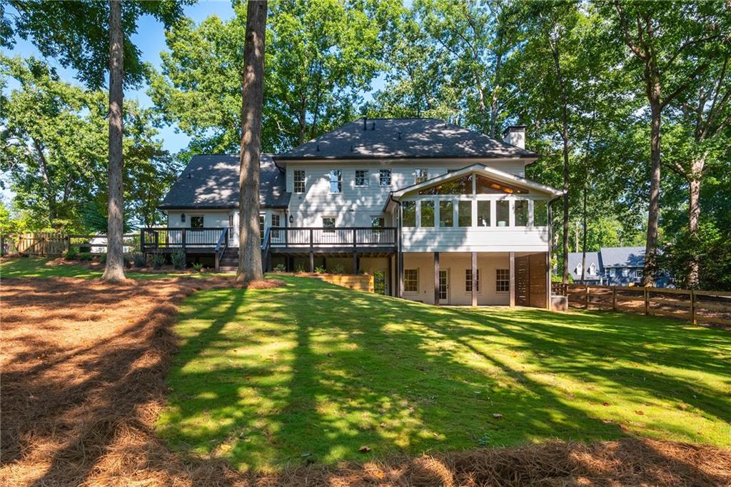 Rear of a two-story home with a raised deck, enclosed sunroom, and tree-shaded lawn.