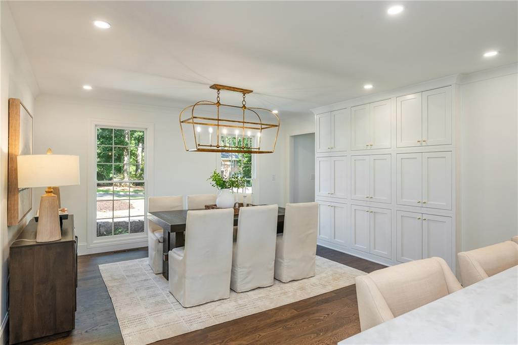 Dining room with white built-in cabinets, a brass chandelier, and windows overlooking greenery.