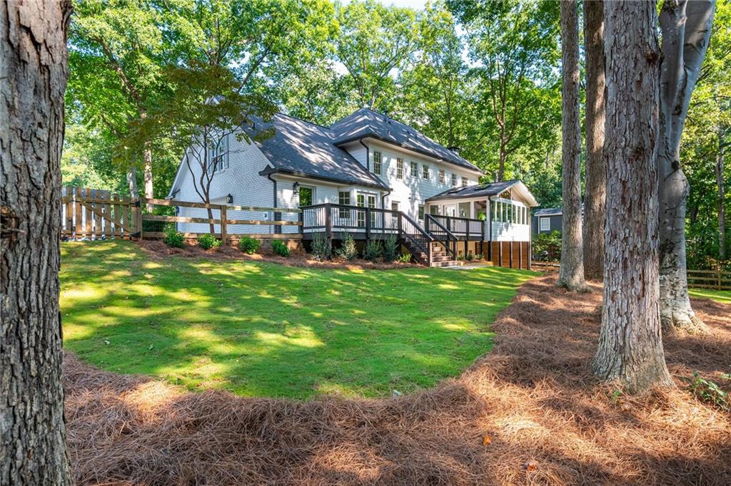White two-story home with a raised deck and broad shaded lawn beneath mature trees.