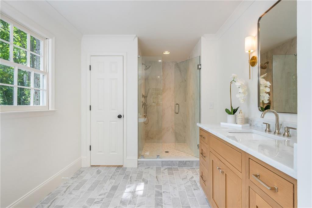 Bathroom with a glass walk-in shower, double vanity, marble-look tile, and a large window.