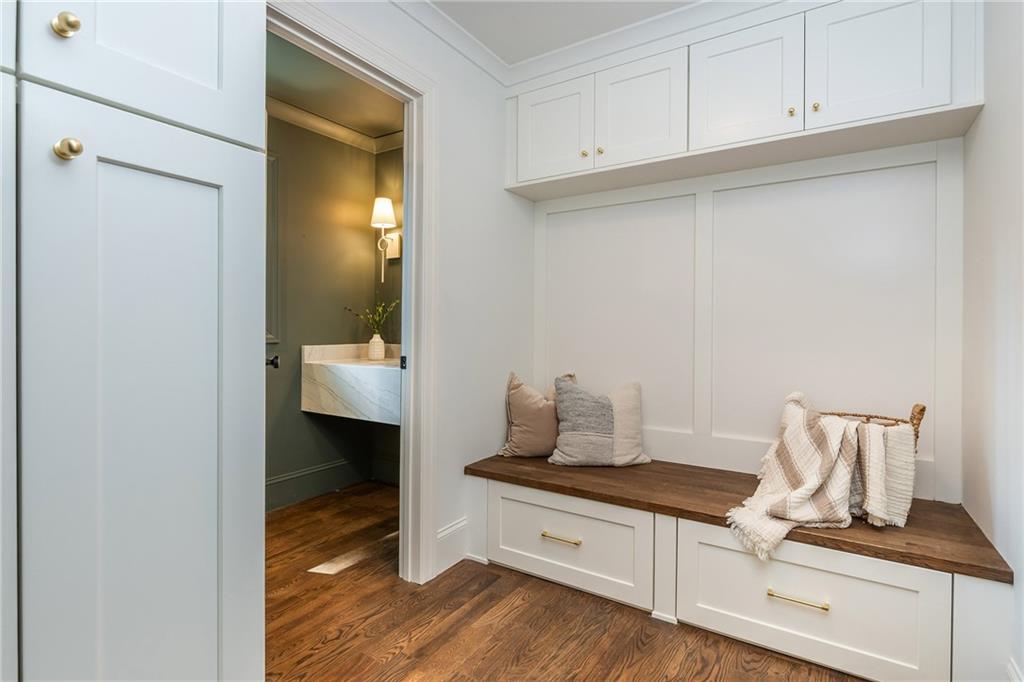 Mudroom with white built-in cabinets and a wood-topped bench beside an open powder room doorway.