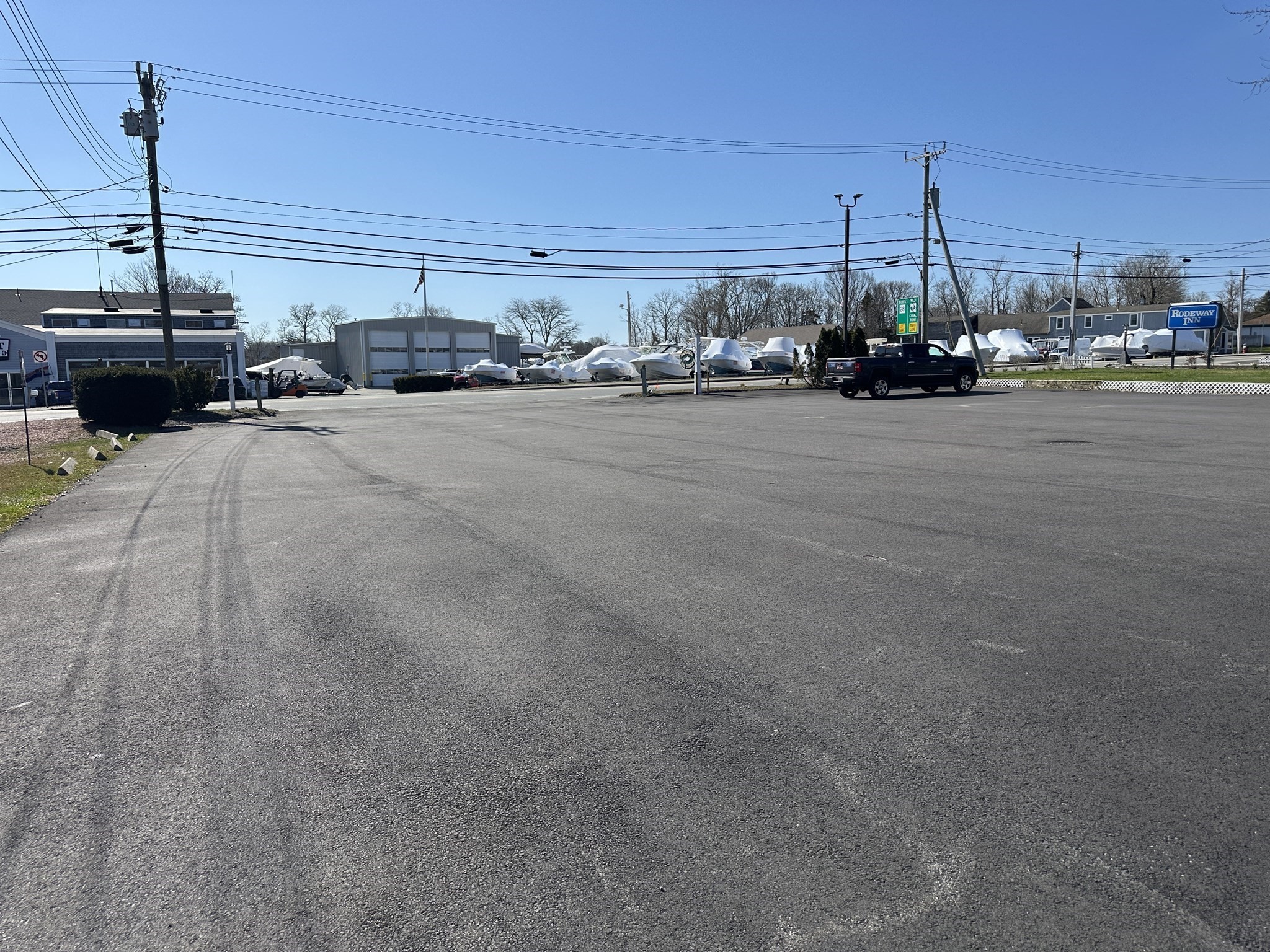 Broad asphalt parking lot with commercial buildings, stored boats, and a Rodeway Inn sign.