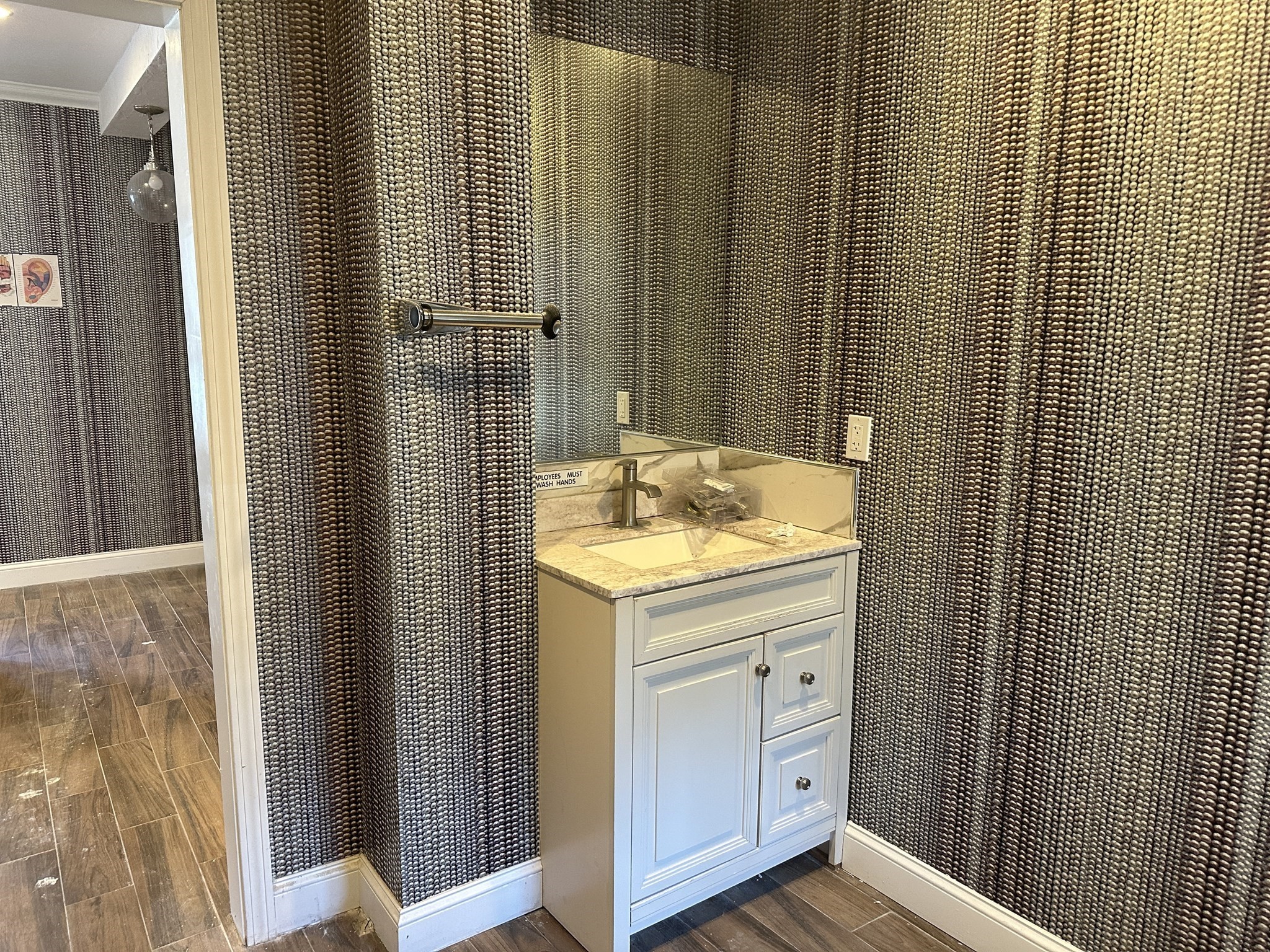 Bathroom vanity with a stone countertop and sink against dark bead-pattern wallpaper.