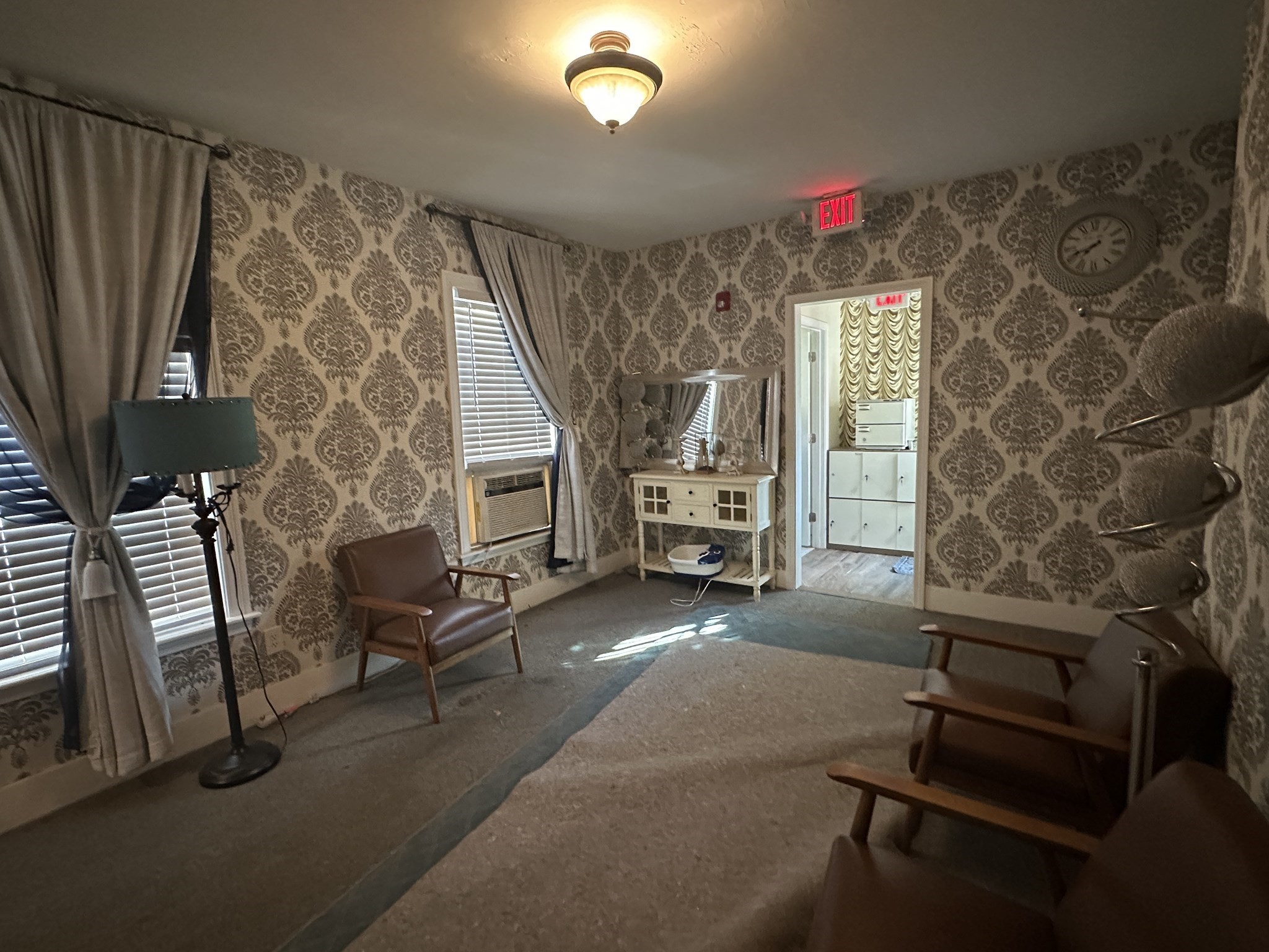 Furnished sitting room with ornate wallpaper, brown armchairs, and sunlight across the carpet.