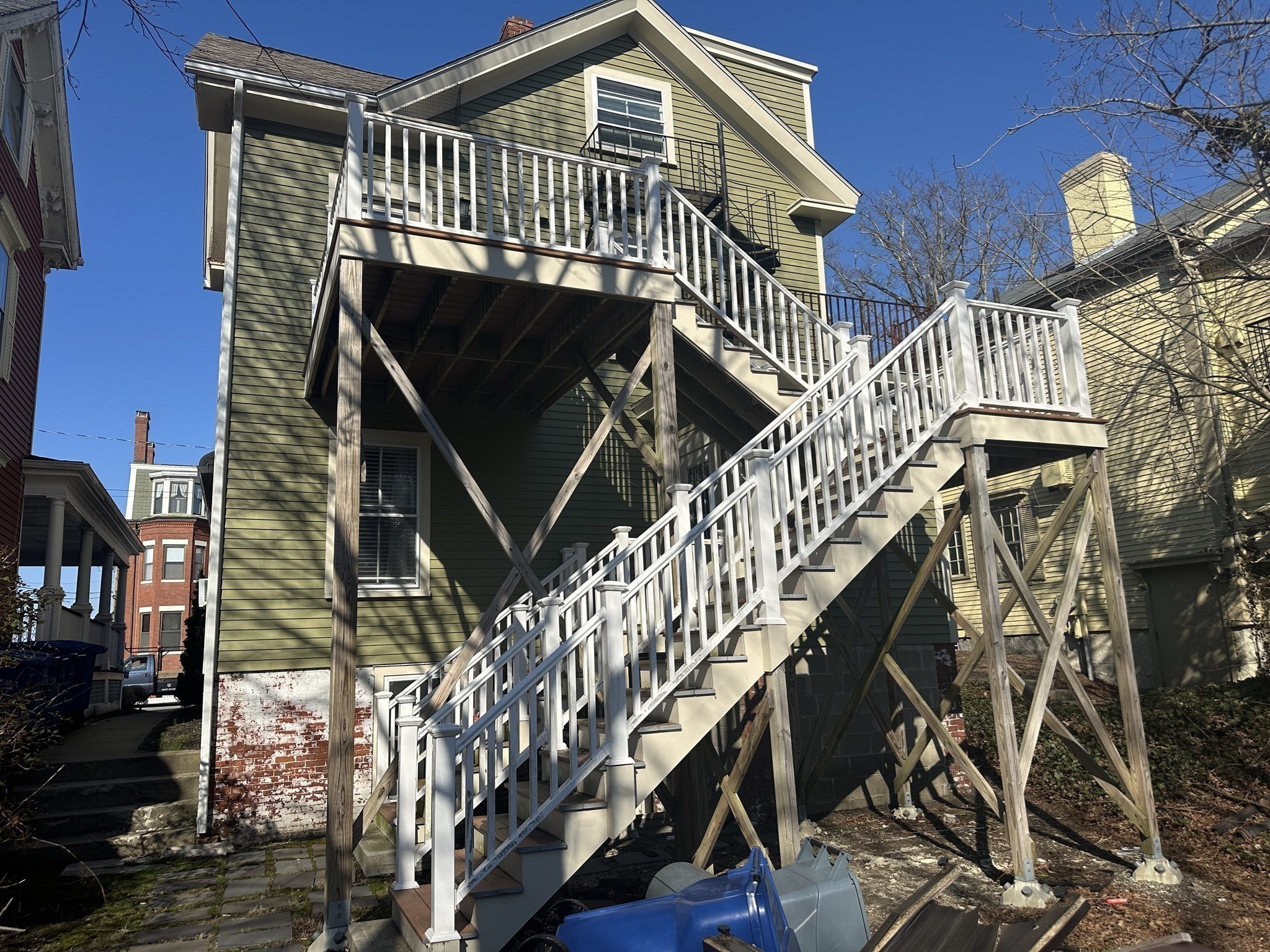 Green-sided home with elevated decks and white-railed exterior staircases on timber supports.