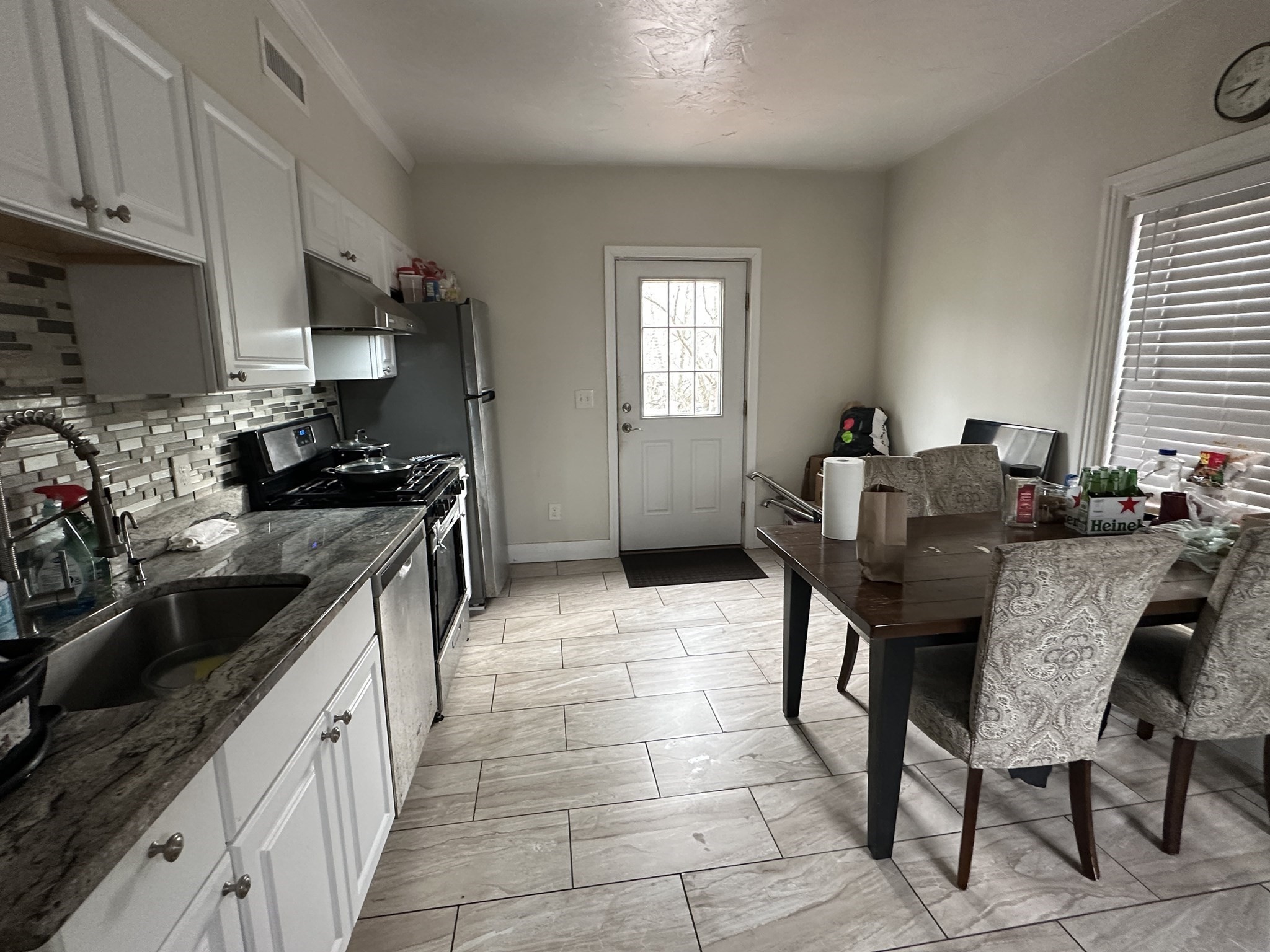 Kitchen and dining area with gray stone counters, stainless appliances, and a dark table with upholstered chairs.