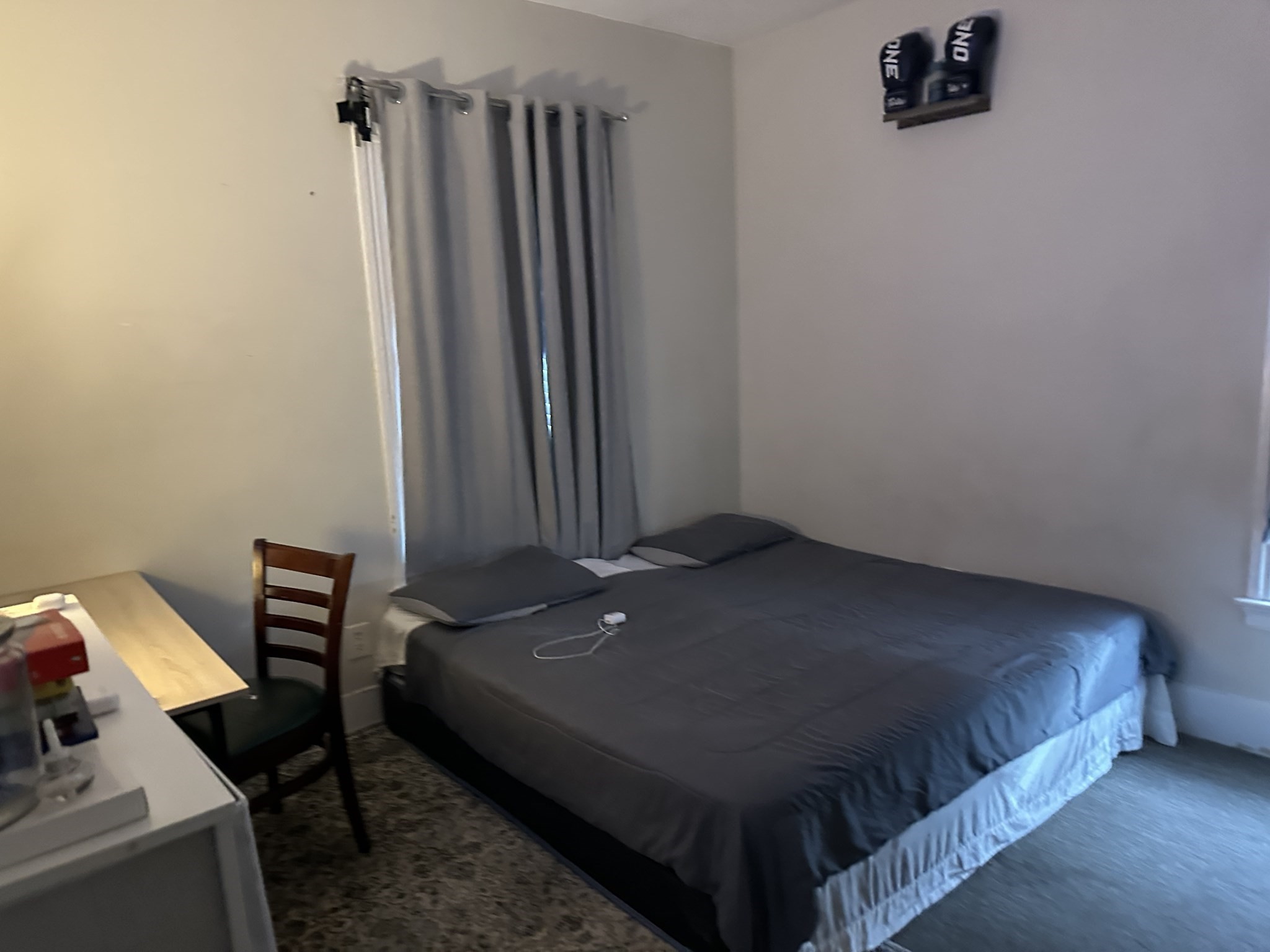 Bedroom with a large dark gray bed, gray curtains, and a small desk and chair.