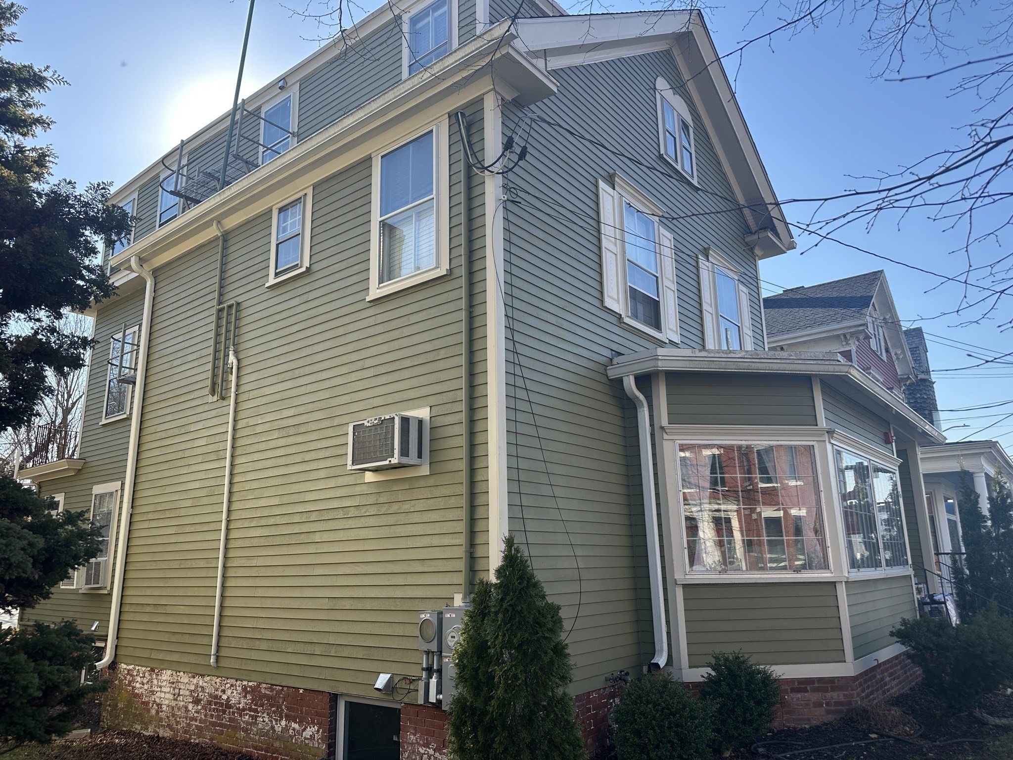 Olive-green multi-story house with white trim, an upper balcony, and a large enclosed porch.