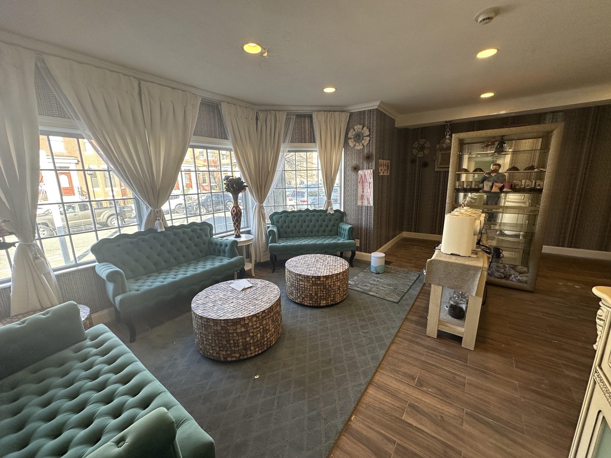Furnished lounge with teal tufted sofas, round tables, and large street-facing windows.