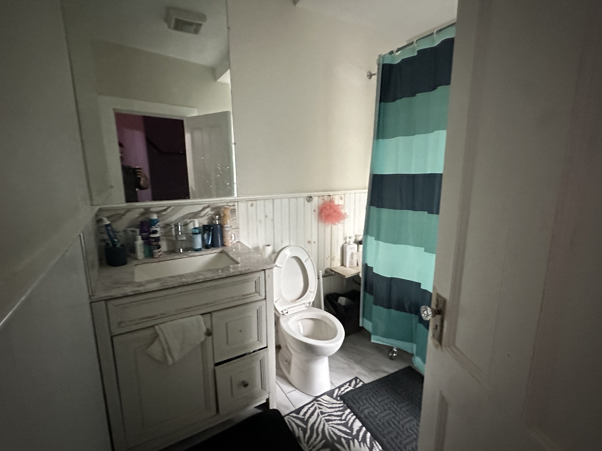 Bathroom with gray vanity, large mirror, toilet, and turquoise and navy striped shower curtain.