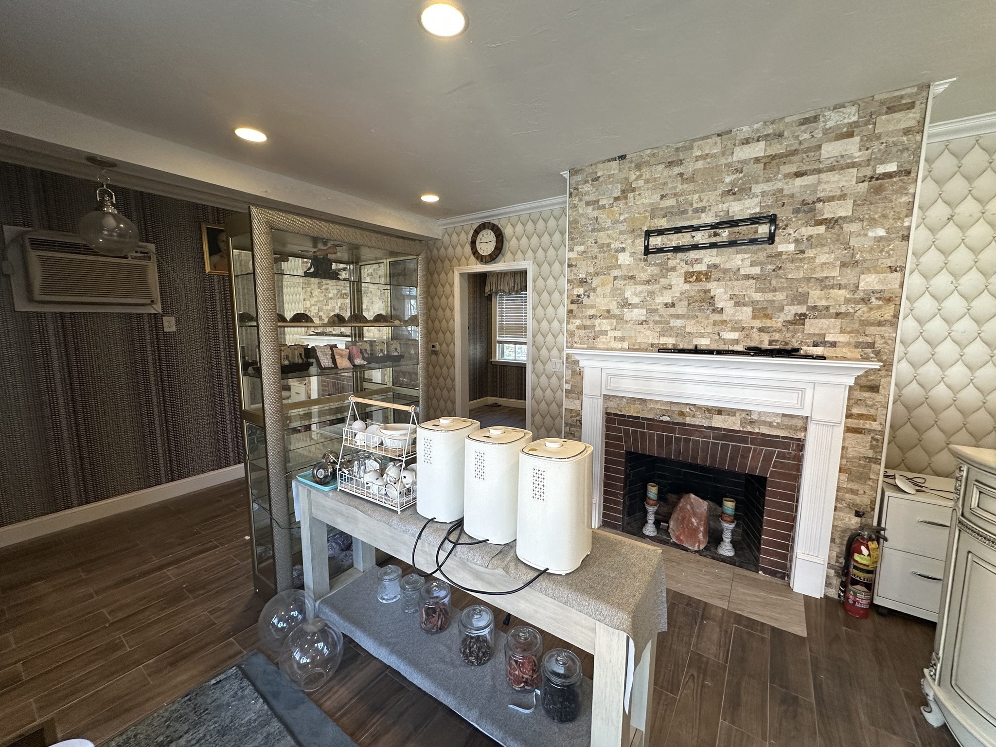 Interior room with a stone-accent fireplace, glass display cabinet, and table of appliances and jars.