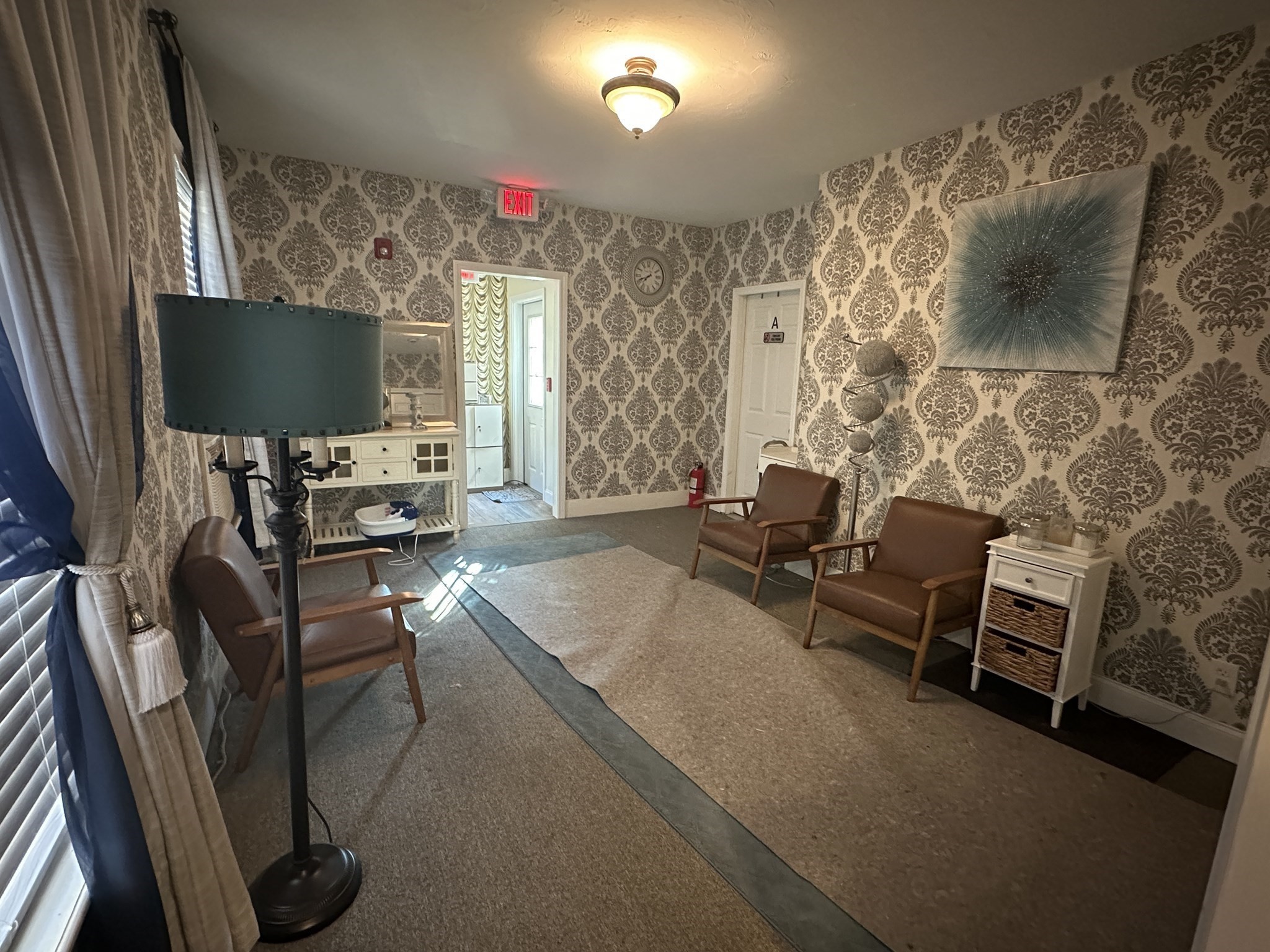 Furnished sitting area with ornate damask wallpaper, brown armchairs, and a large rug.