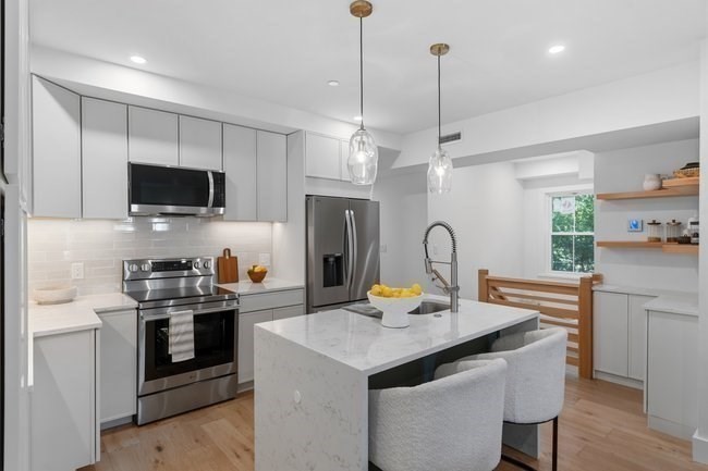 Modern white kitchen with a marble-look island, stainless steel appliances, and a dining nook.
