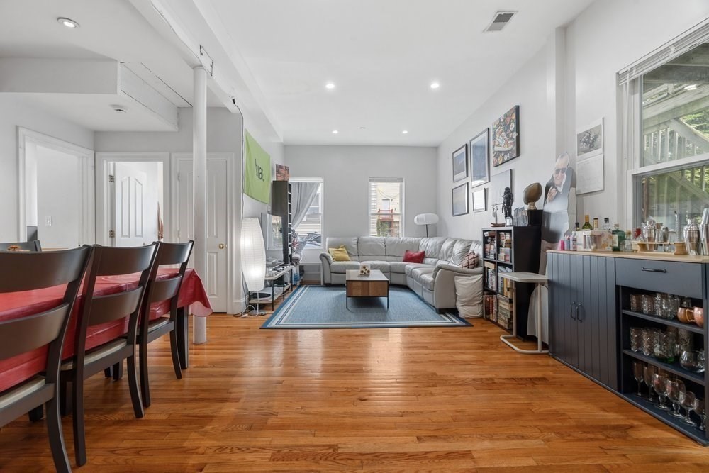 Open-plan living and dining room with hardwood floors, gray sectional, and dark blue kitchen peninsula.