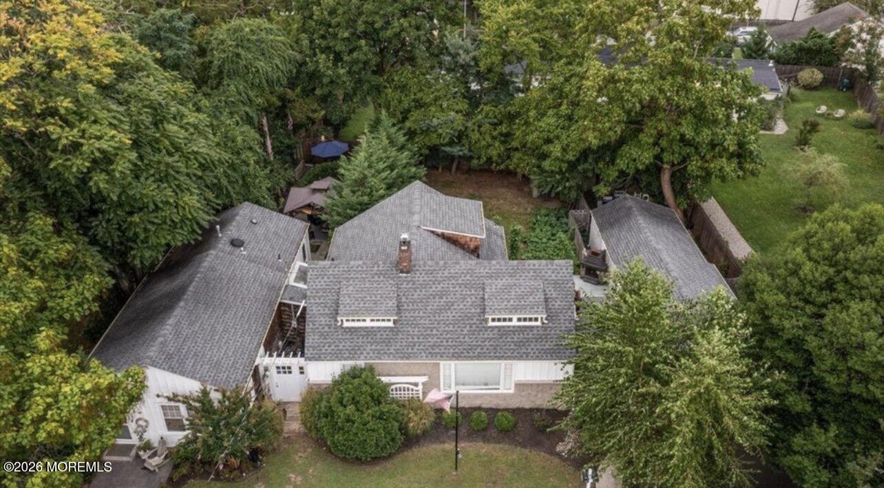 Aerial view of a gray-roofed home surrounded by mature trees and landscaped grounds.