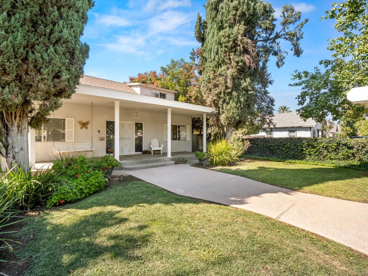Single-story home with a covered porch, mature trees, landscaped beds, and a curved walkway.