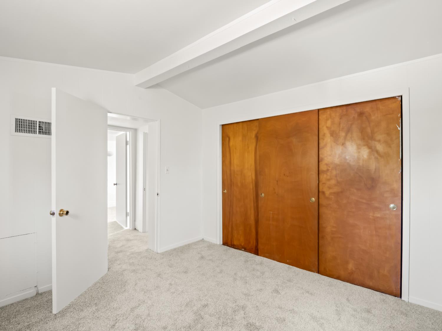 Empty bedroom with light carpet and large wooden sliding closet doors.