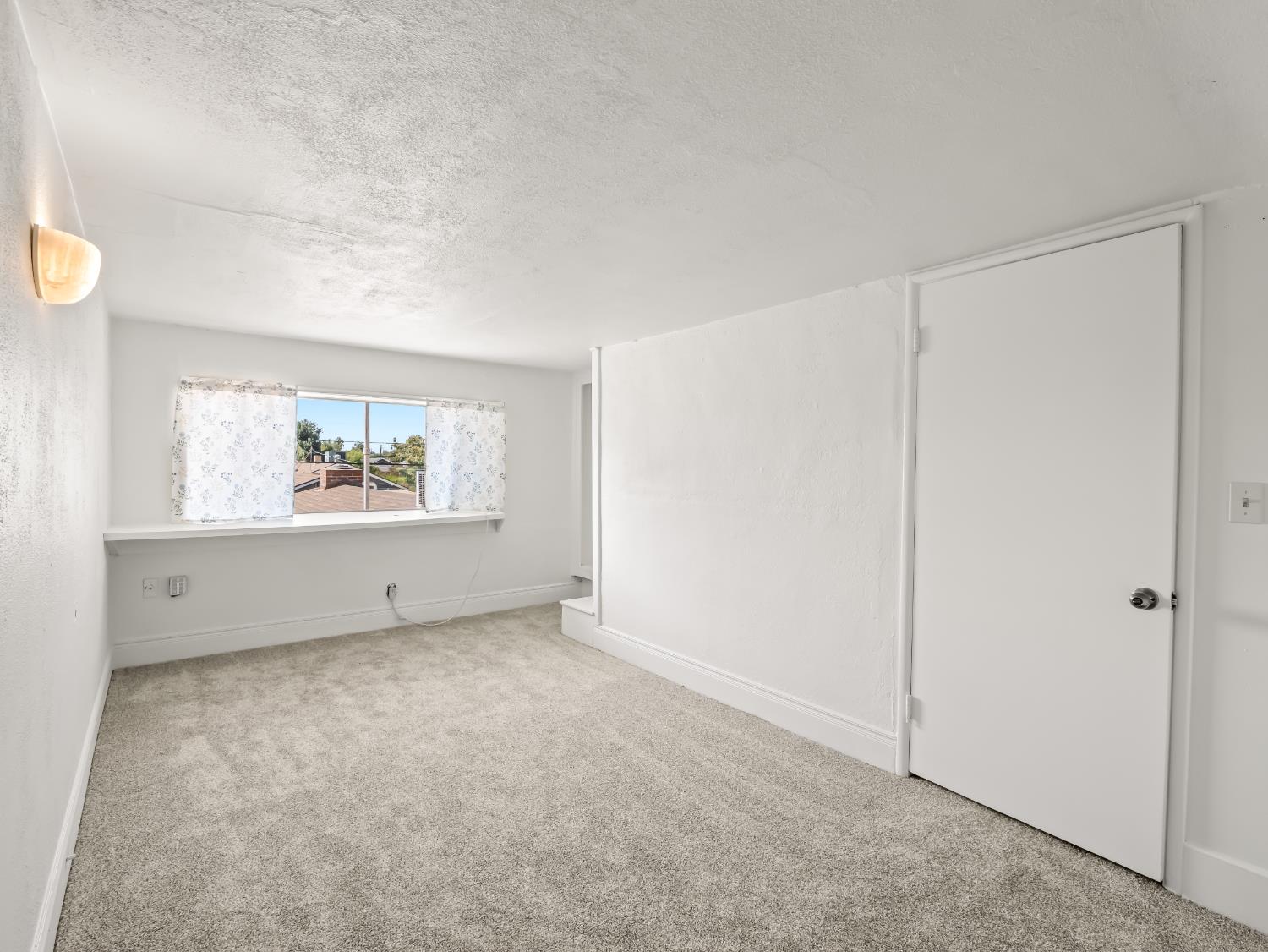 Empty carpeted room with a curtained window and a wall partition.